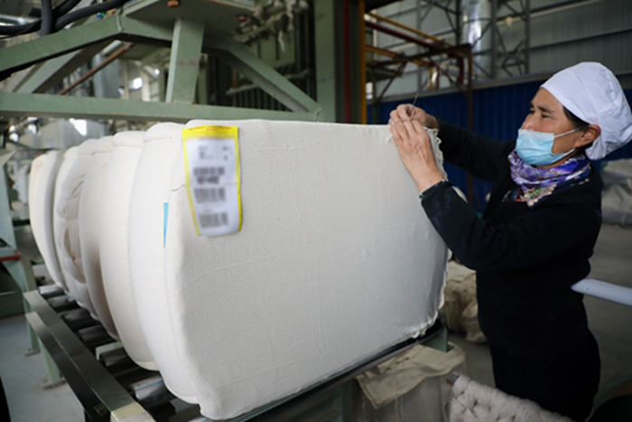 早日复工复产，棉花加工厂女工正在缝合棉包.png
